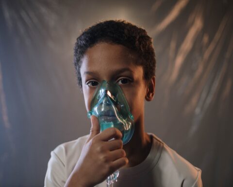a boy in white shirt holding green oxygen mask